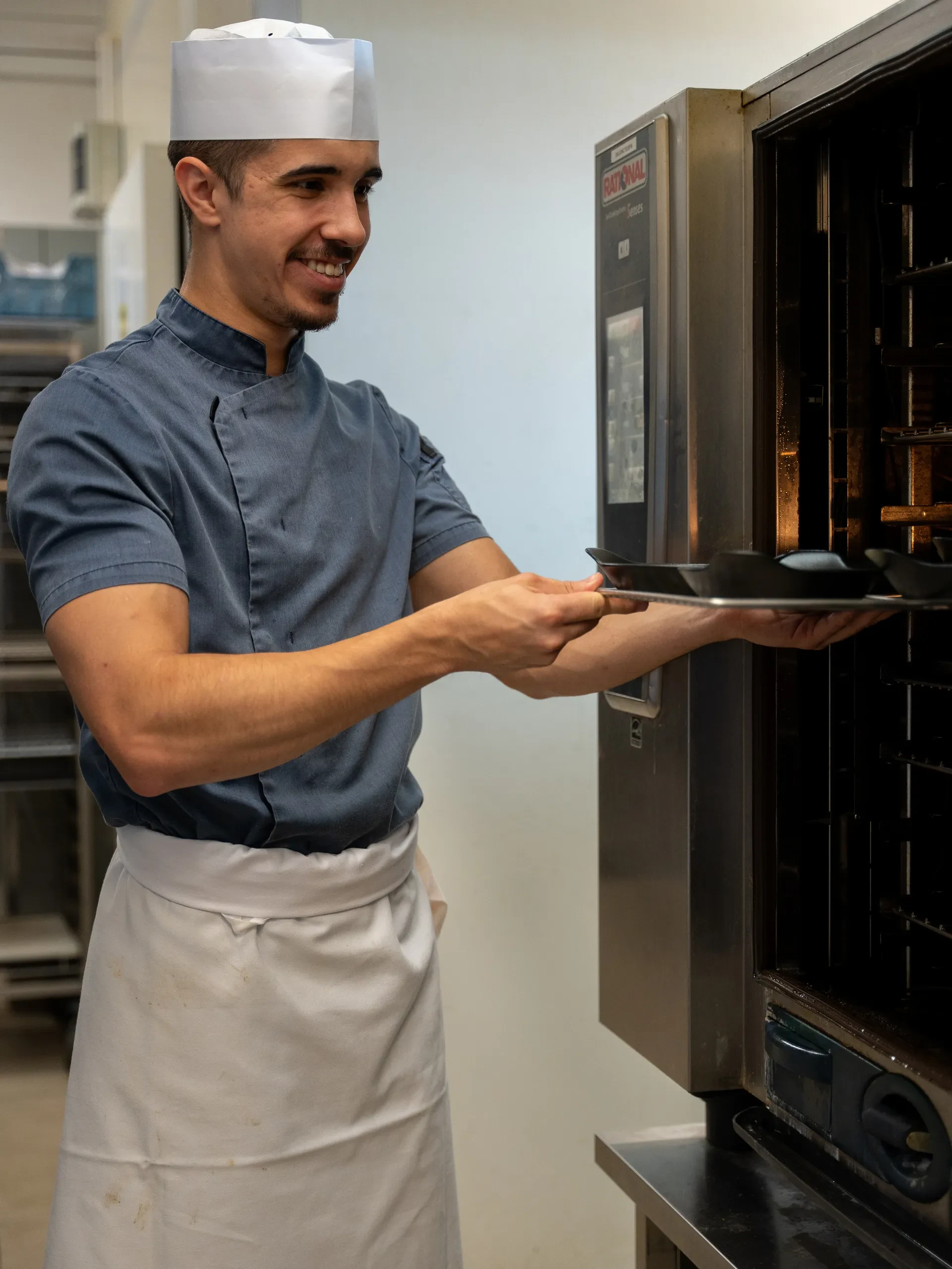 Chef souriant cuisinant avec un four industriel.
