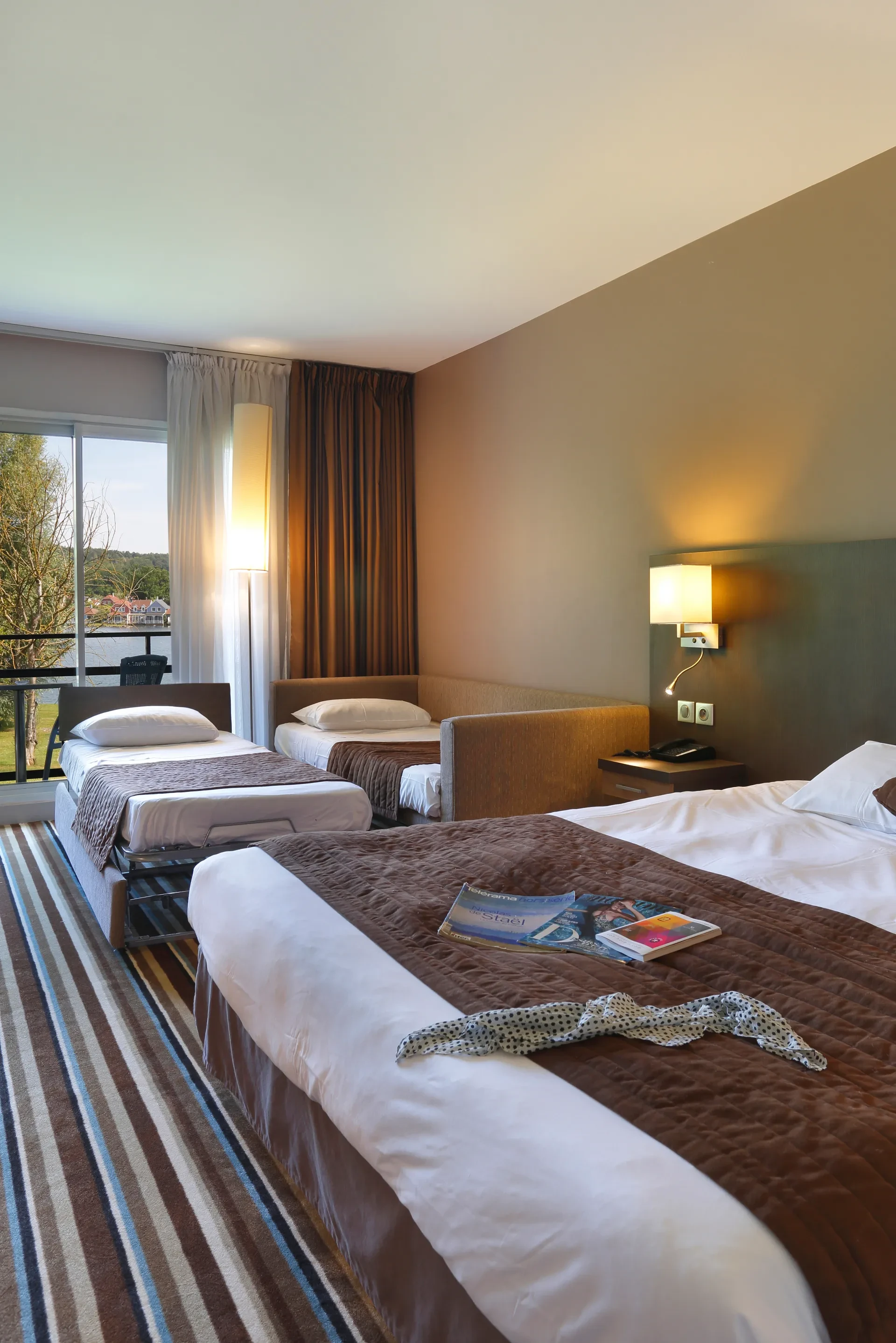 Chambre d'hôtel avec trois lits et vue extérieure.