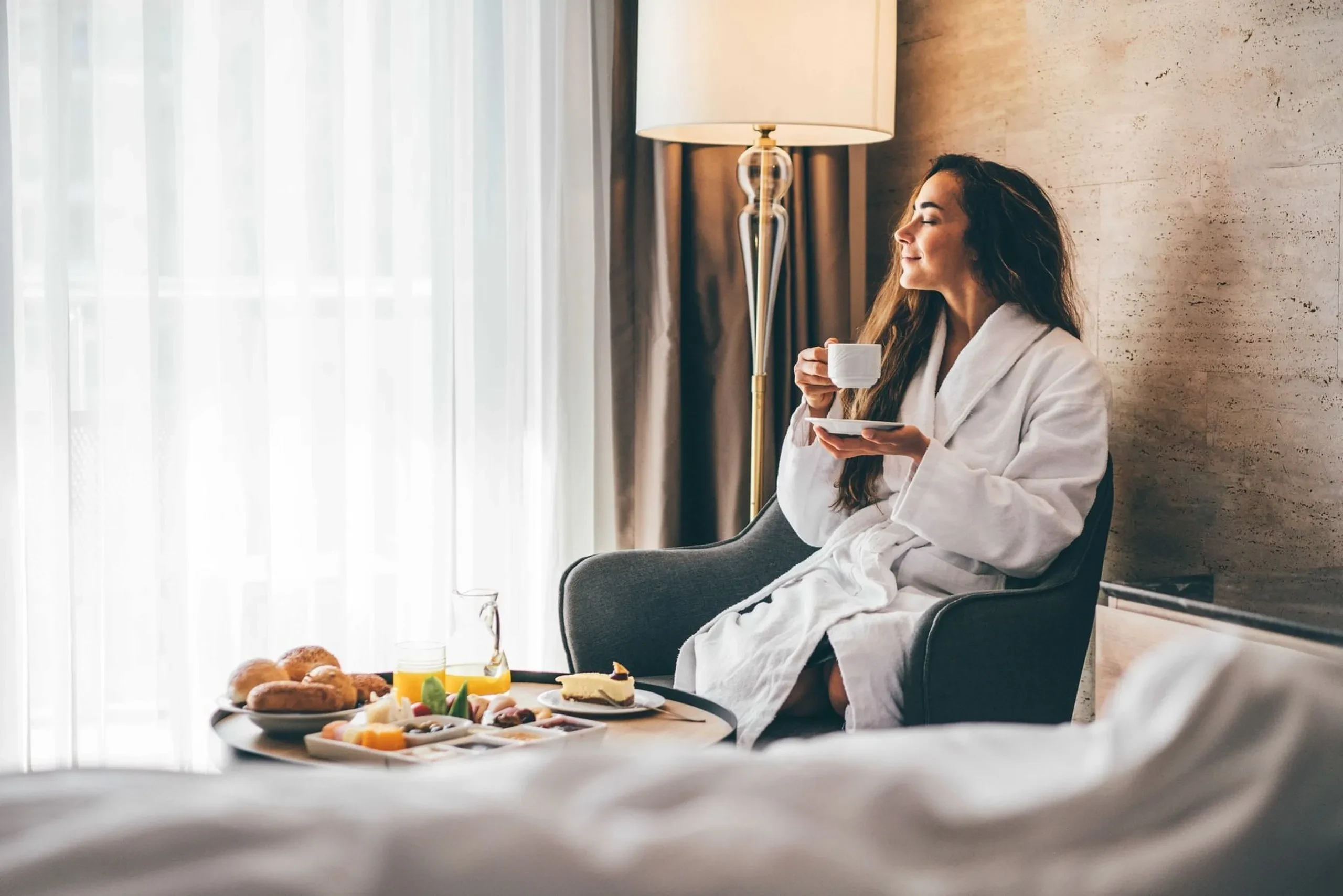 Femme assise sur un lit d'hôtel profitant d'un petit-déjeuner avec vue.