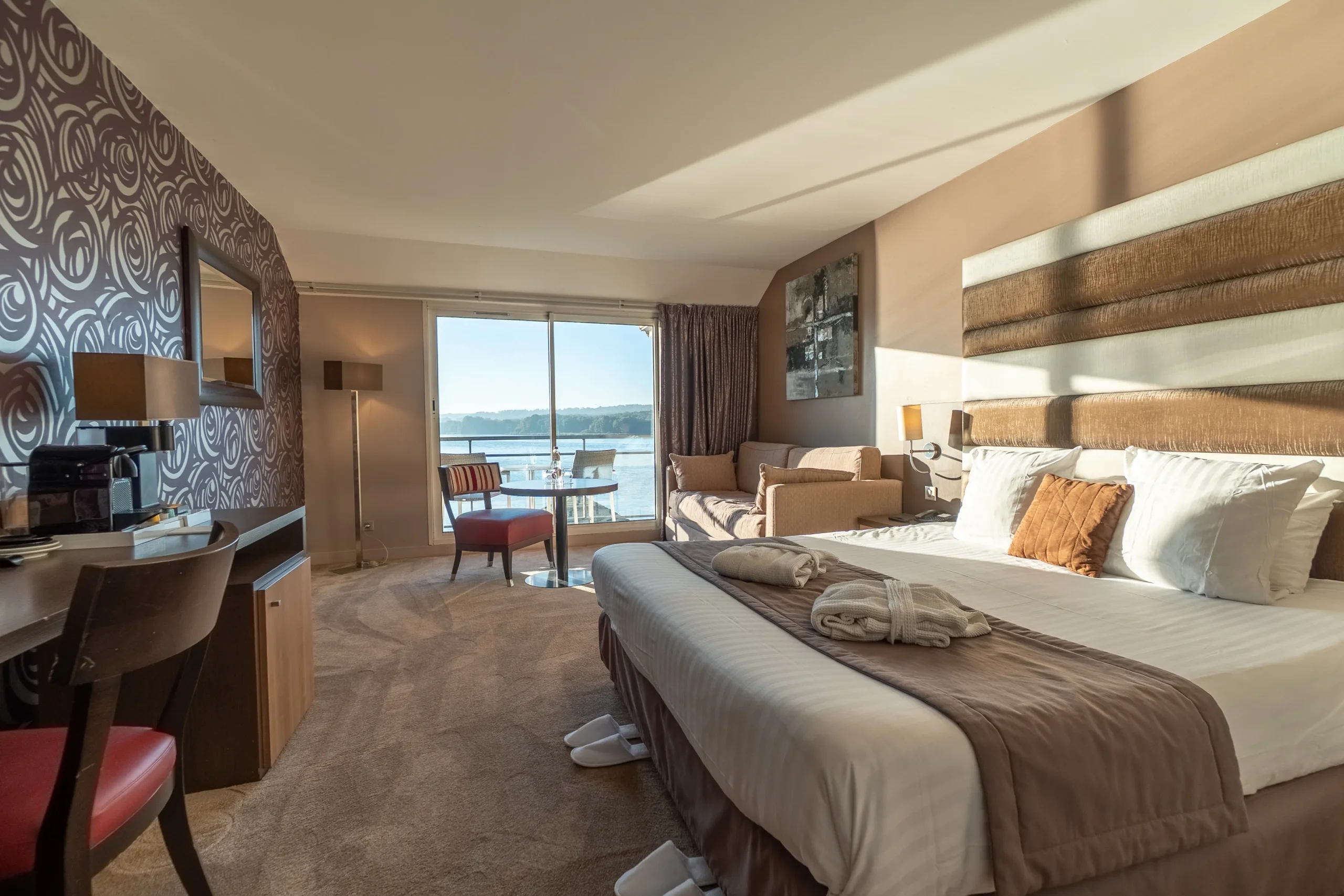 Chambre d'hôtel moderne avec grand lit double, espace bureau et vue panoramique sur l'eau.