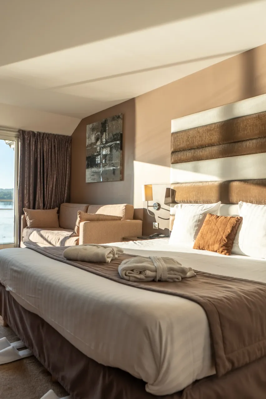 Vue d'ensemble d'une chambre spacieuse incluant le lit, un espace salon et une grande fenêtre.