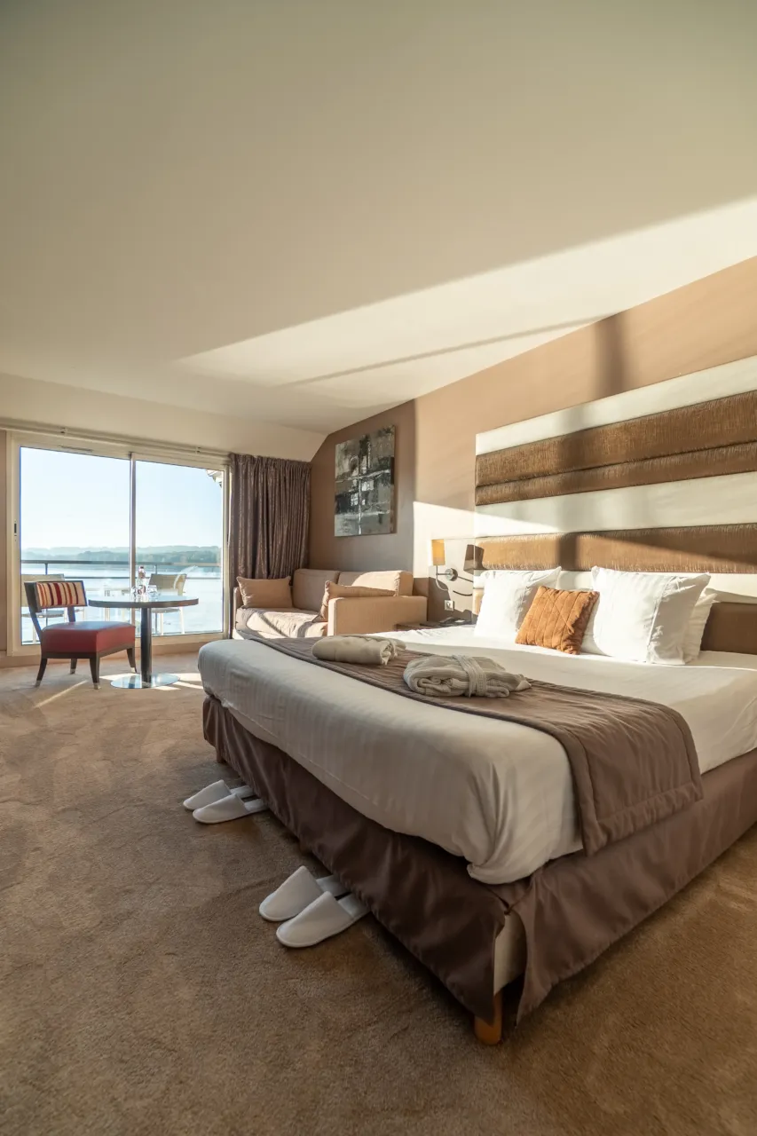 Grande chambre d'hôtel moderne avec lit double king-size, décoration épurée et baie vitrée.