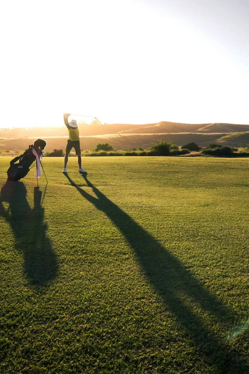 Golfeur pratiquant un swing au coucher du soleil.