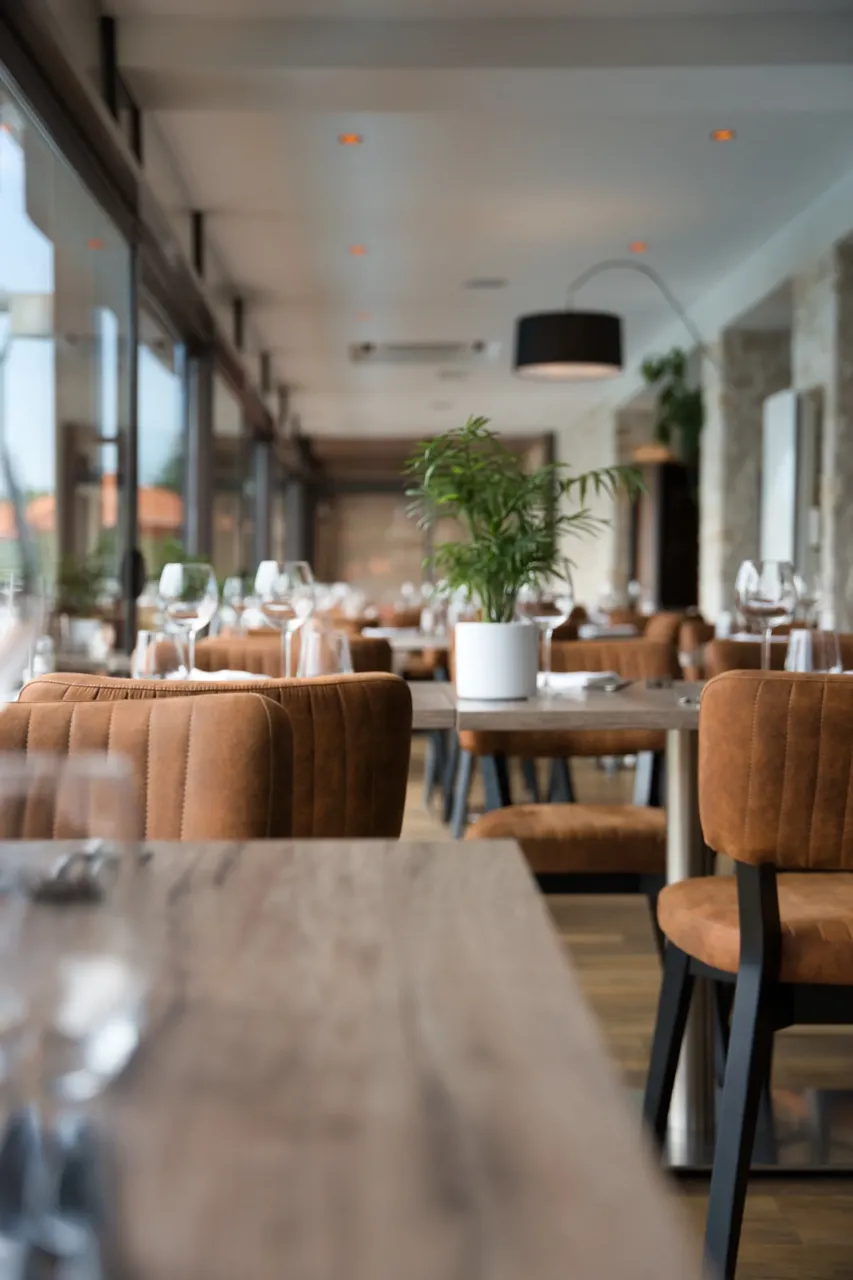 Intérieur lumineux d'un restaurant moderne avec fauteuils en cuir marron et plantes vertes.