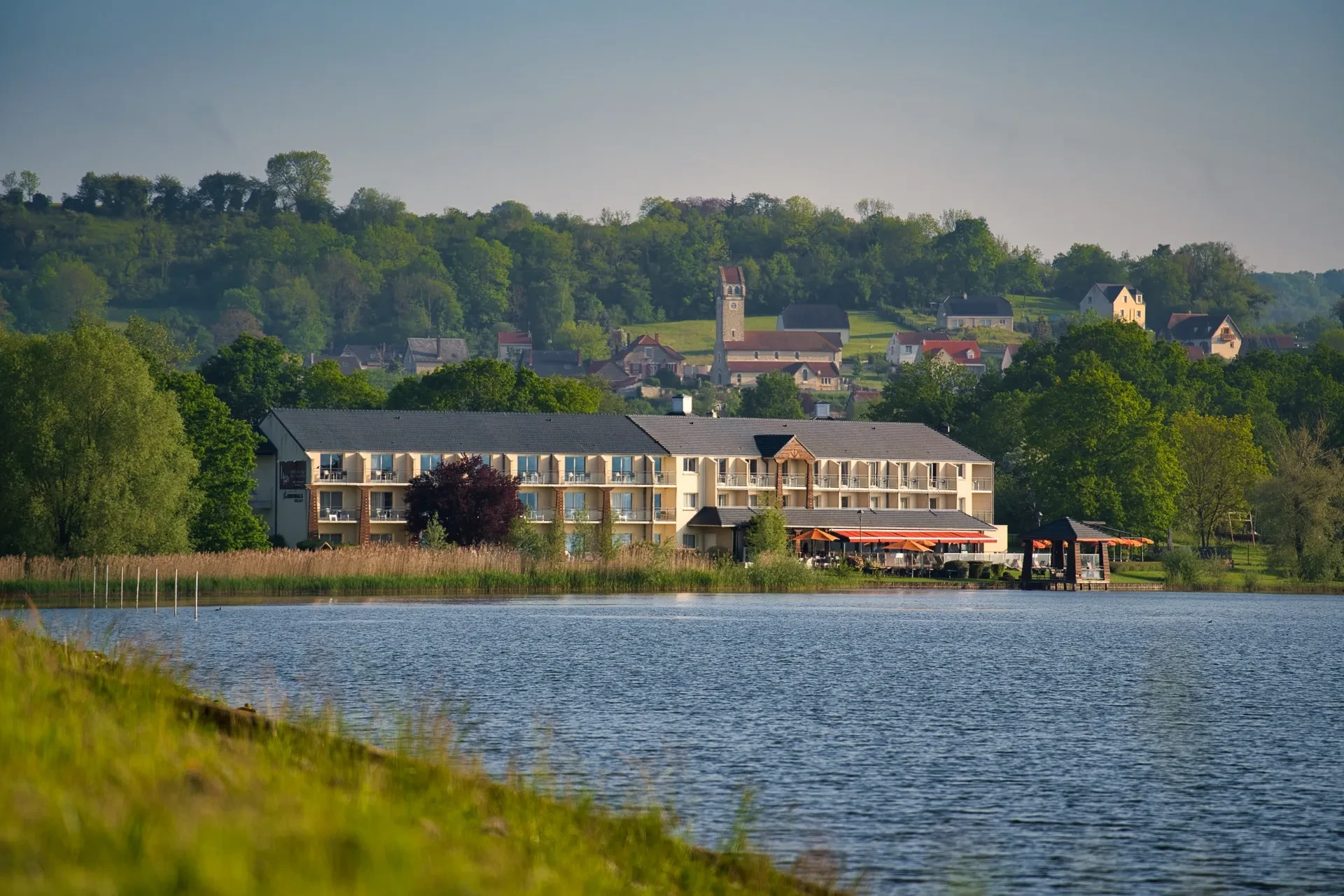 Hôtel au bord d'un lac avec village en arrière-plan.